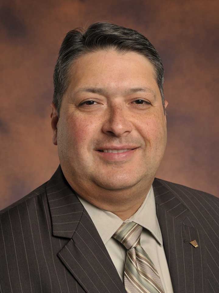 Man in a gray pinstripe suit with a beige shirt and tie smiling