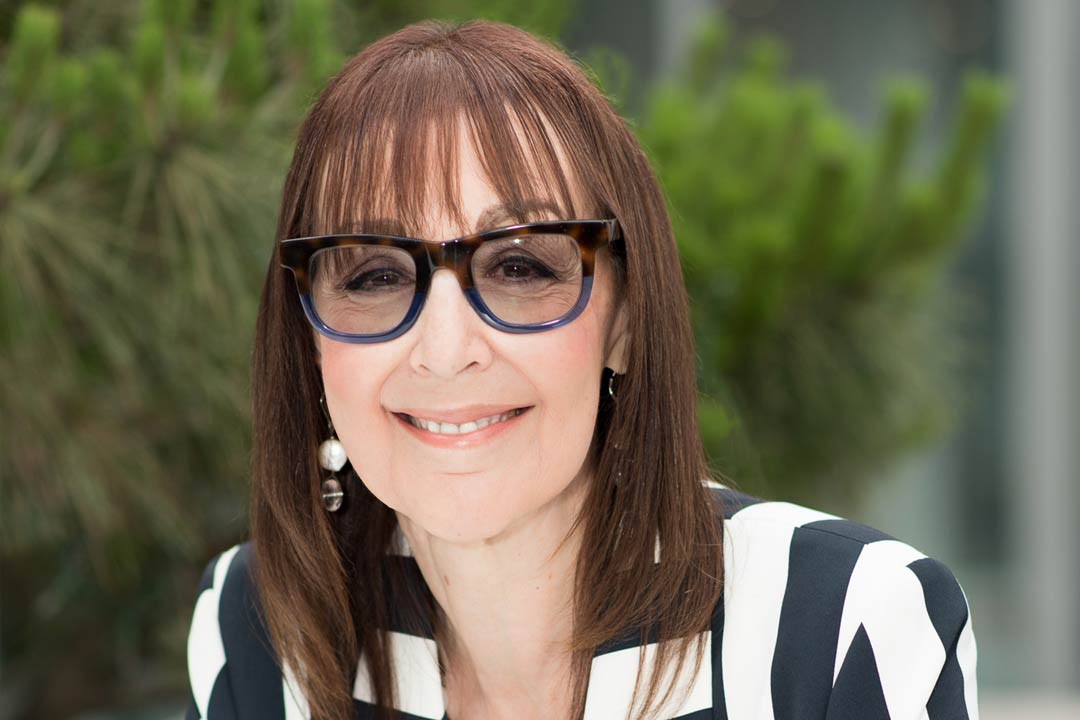 Woman in a black and white striped jacket with brown long hair and glasses smiling broadly