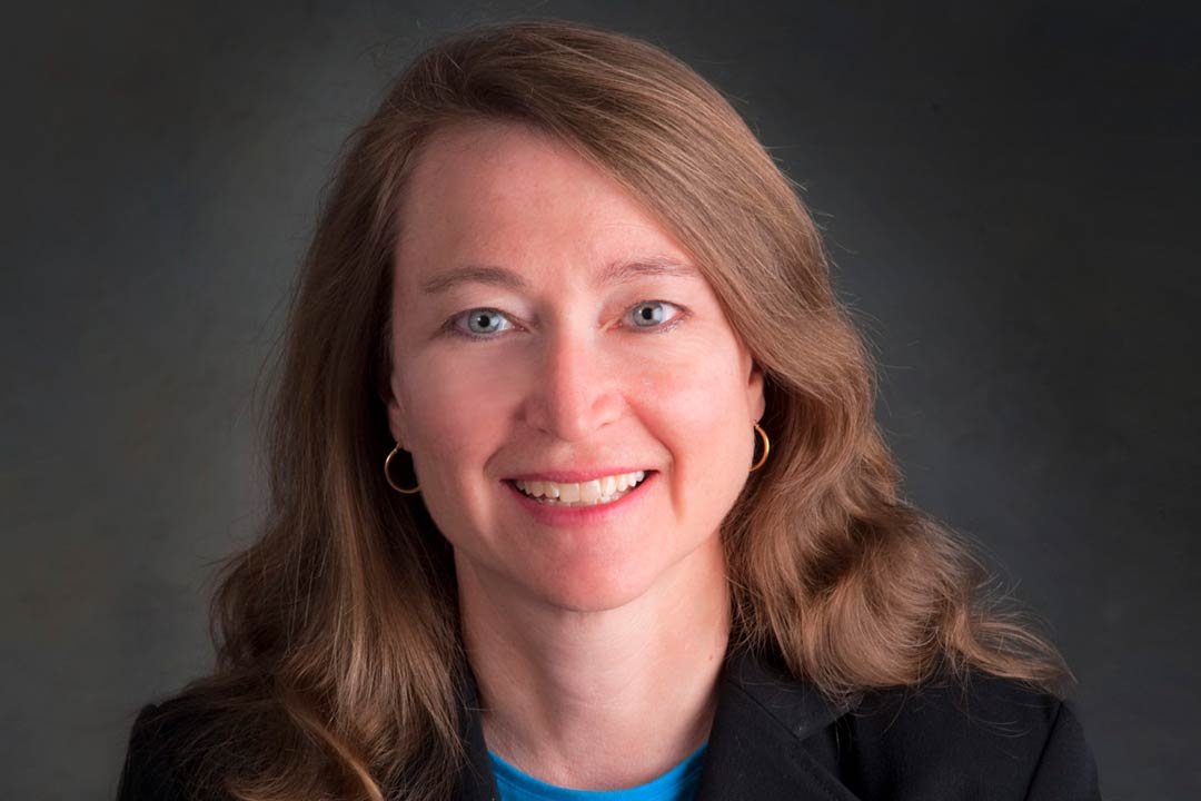 Woman in a dark jacket with shoulder length light brown hair smiling and looking straight ahead