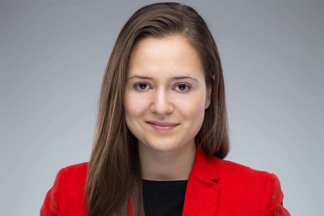 Woman with long brown hair pulled to one side in a bright red jacket smiling and looking straight ahead