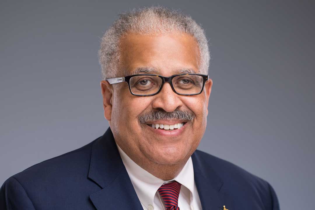 Man in a blue suit with gray hair, glasses and a broad smile