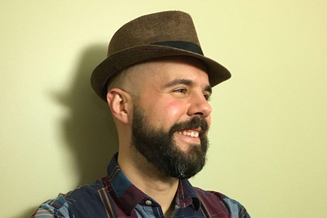 Man with a beard and wearing a hat looking right and smiling