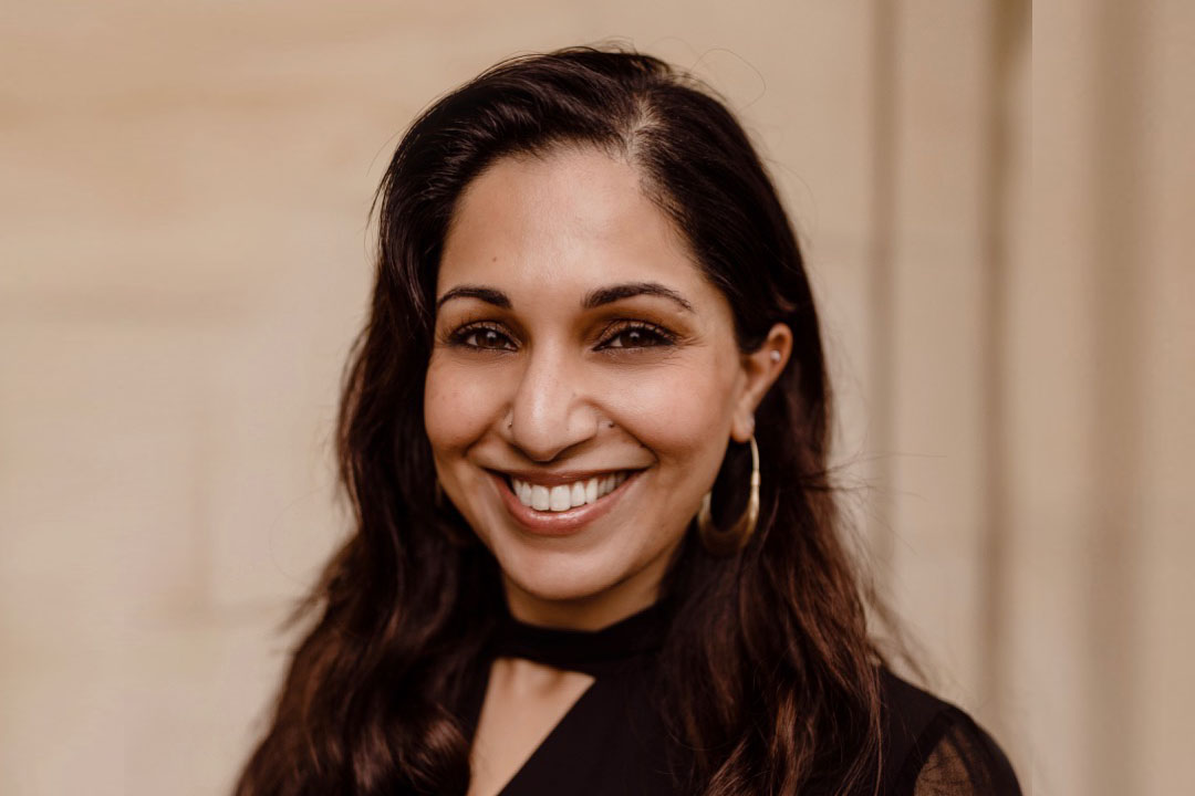 Headshot of a woman with long dark hair and a dark shirt and a very broad smile