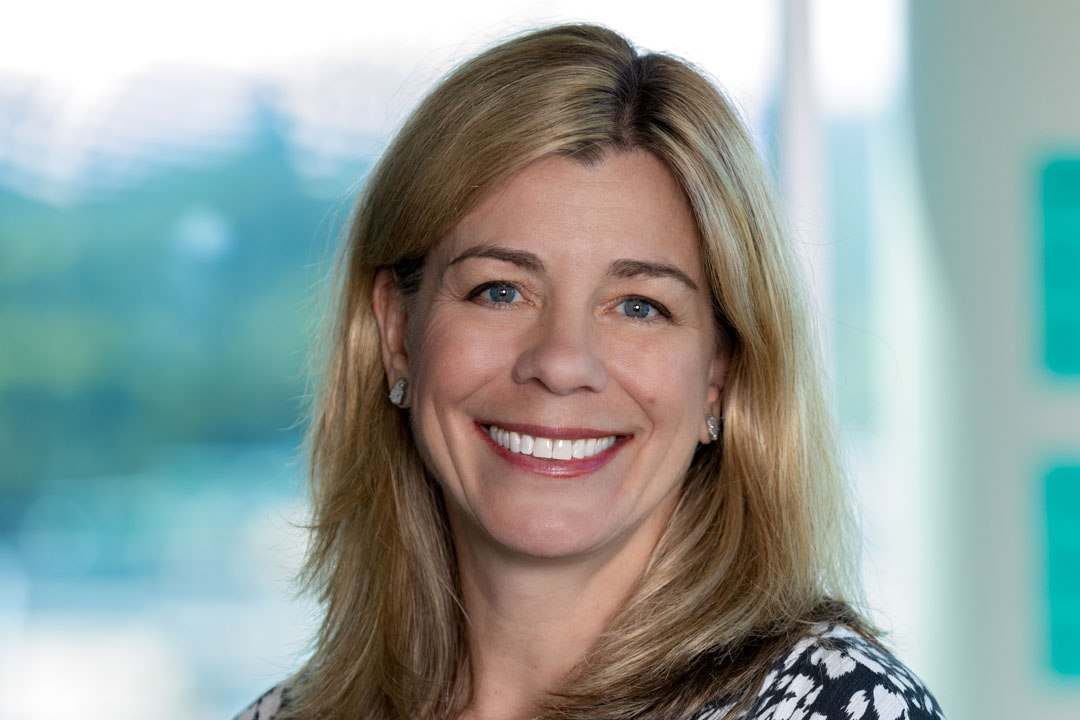 Headshot of a woman with a flowered shirt and blonde shoulder length hair smiling broadly