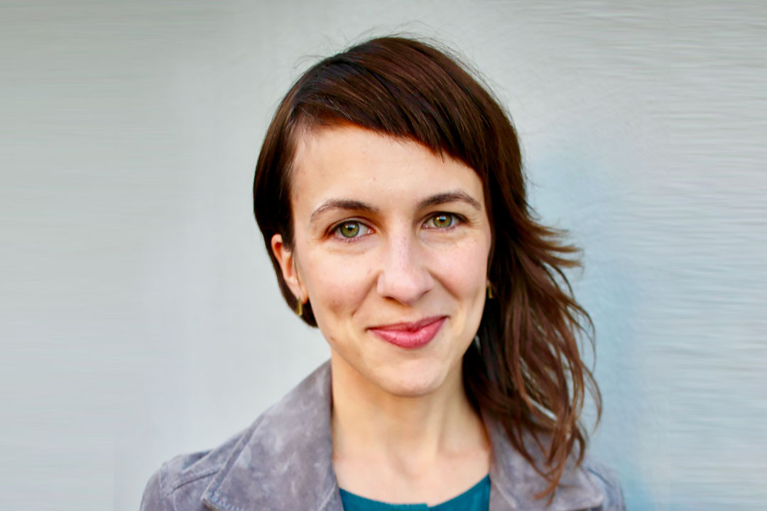 Headshot of a woman with shoulder length brown hair and a gray jacket smiling