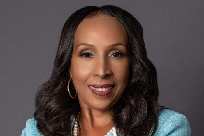 Woman with a broad smile wearing a light blue jacket and pearl necklace