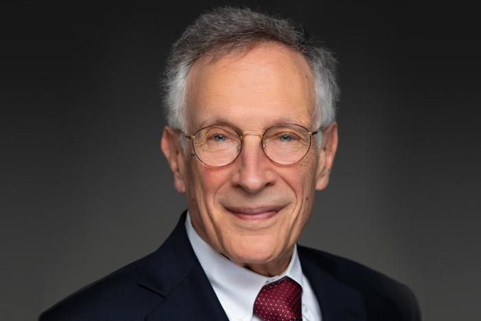 Man with glasses in a dark jacket with a white shirt and dark tie smiles and looks into the camera