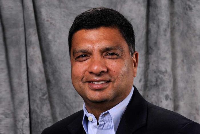 Man in a dark jacket with a light blue shirt smiling