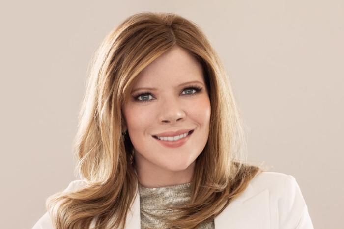 Woman with long hair and a light jacket smiling broadly