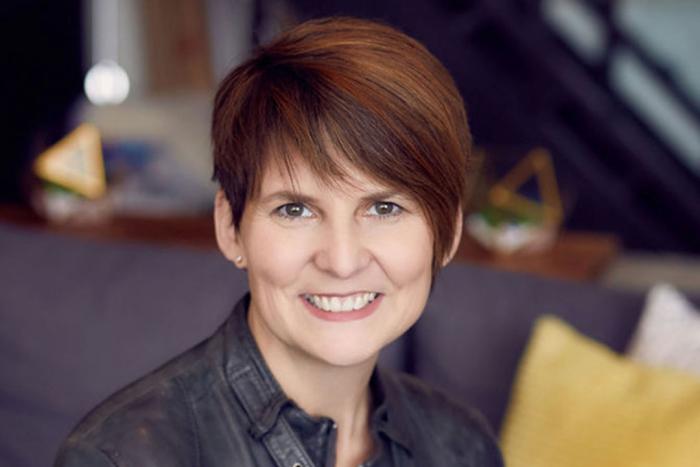 Woman with short hair and a dark jacket smiling broadly
