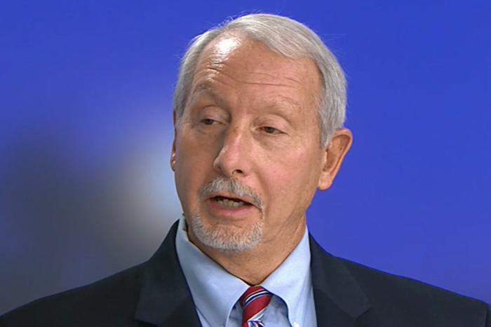 Man with a light blue shirt, striped tie and dark jacket looking aside and talking