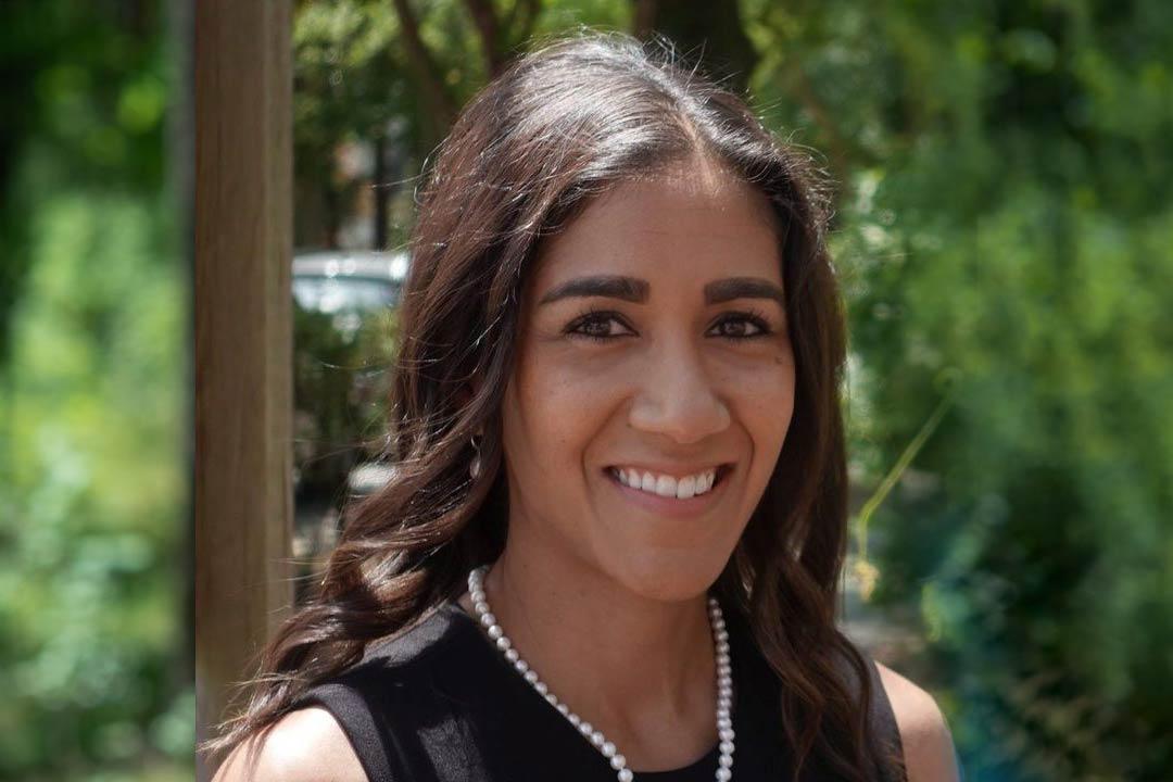 Woman with brown hair smiling with a background of trees
