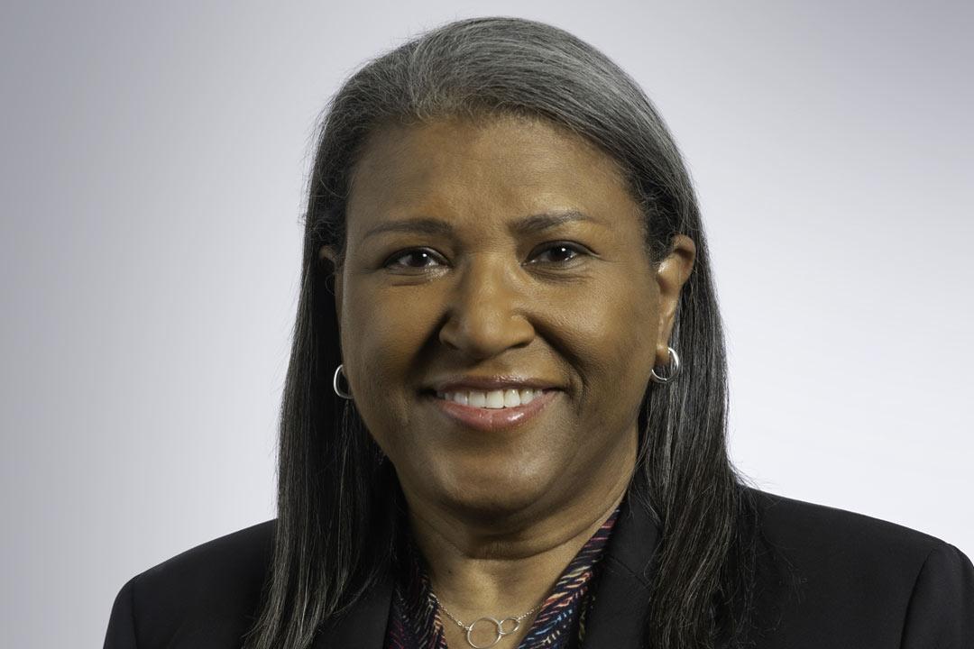 Woman with shoulder length hair, a dark green jacket and a broad smile